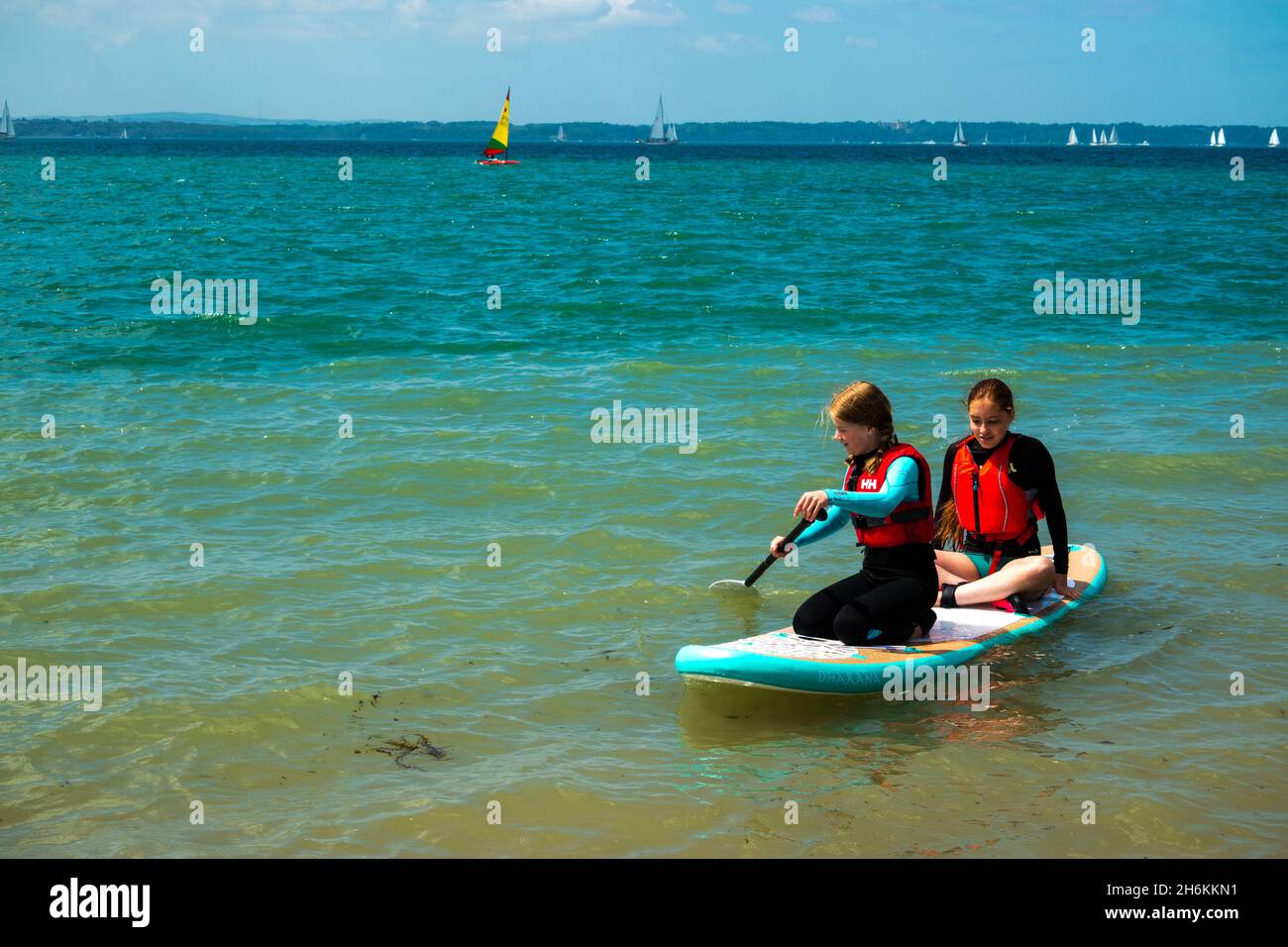 Two girls wearing lifejackets on a paddleboard on the Solent near