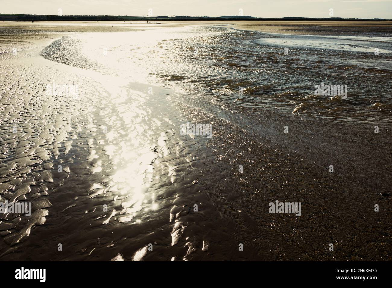 Sun shining and shimmering on the wet sand at Brancaster beach North Norfolk England Stock Photo