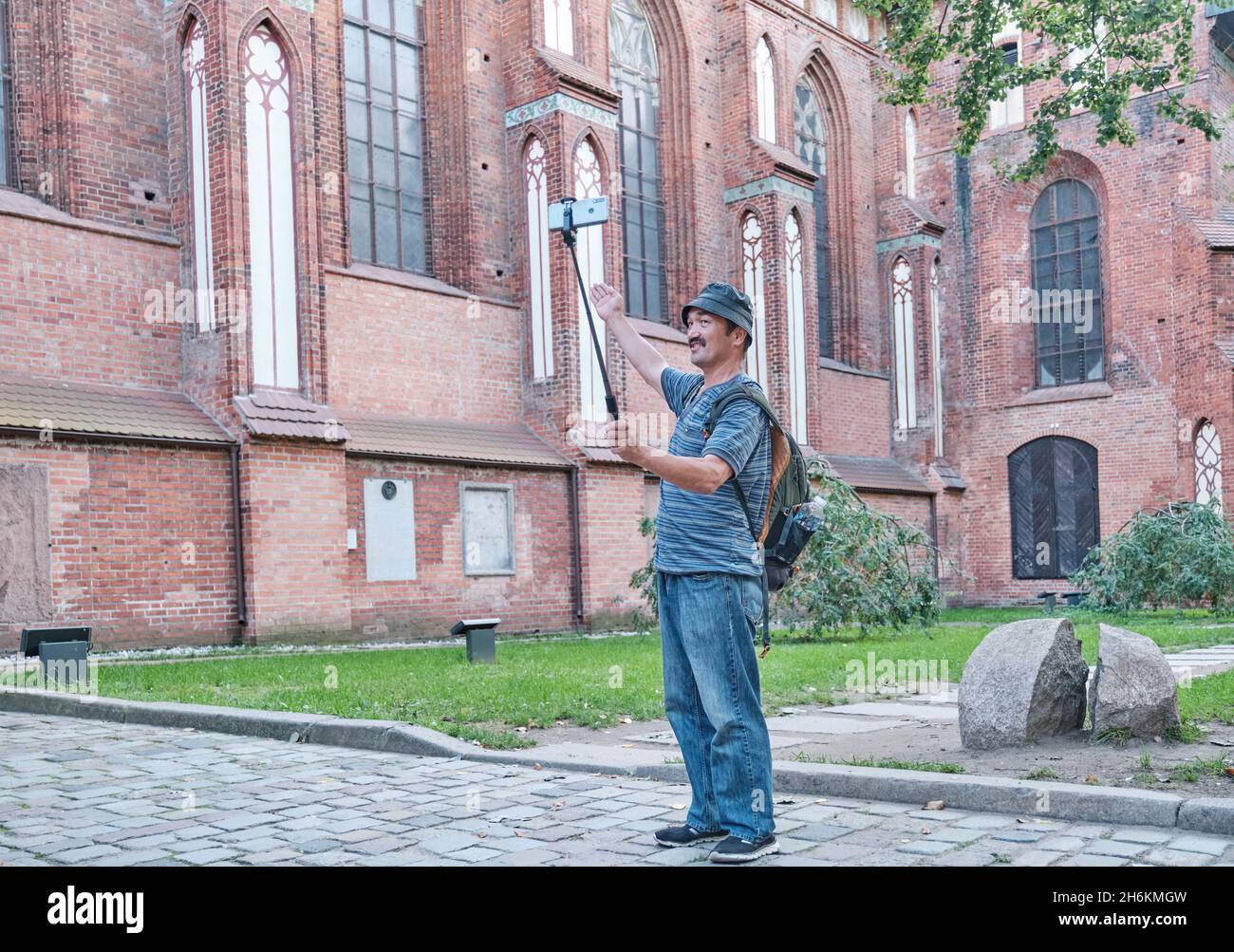 Senior Asian man shooting video by mobile phone for his blog on social network near Cathedral, Kaliningrad, Russia. Stock Photo