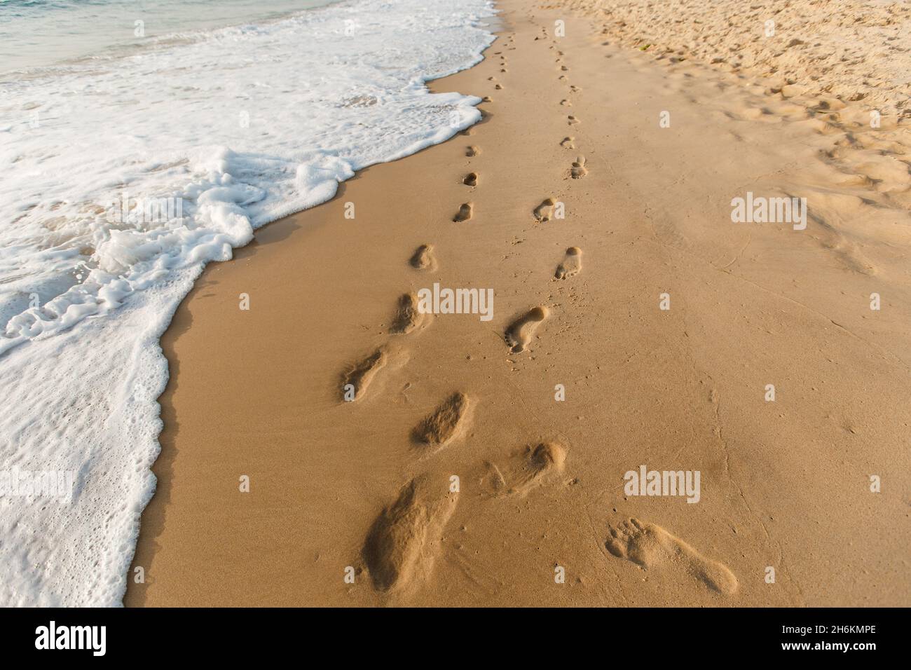 Two footprints ways on the sand. Ocean waves wash away people's tracks. Concept of honeymoon and walking on the summer beach Stock Photo