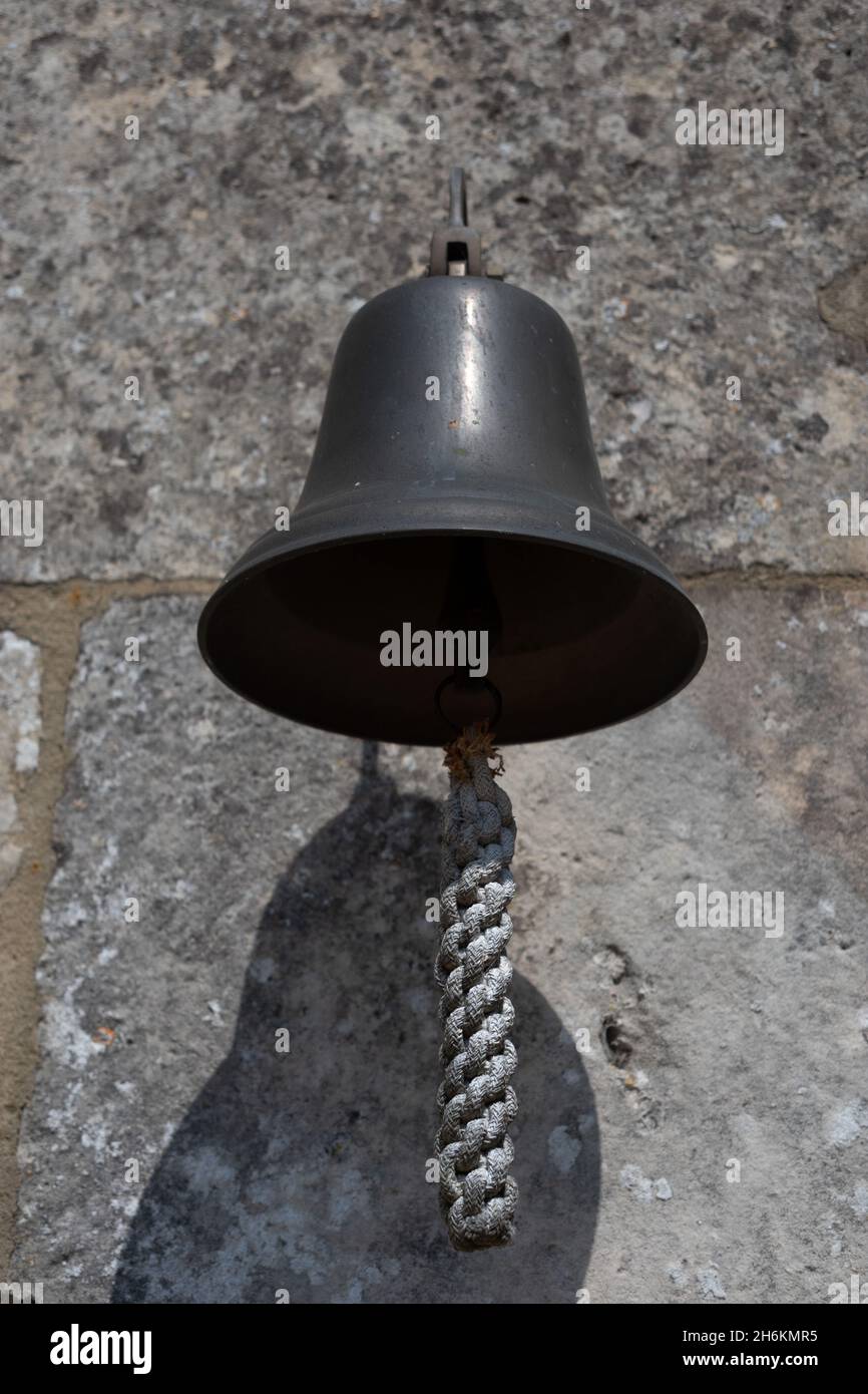Close up of a small bell with lanyard hanging from a wall Stock Photo