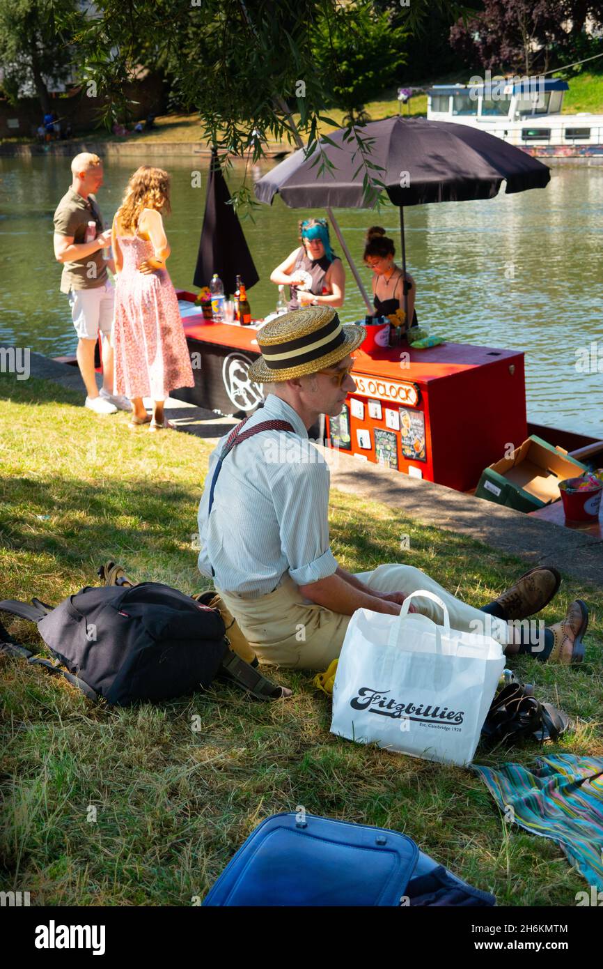 Floating punt Pimms bar on the River Cam with man in old fashioned retro clothing and vintage straw boater hat with picnic from Fitzbillies bakery Stock Photo