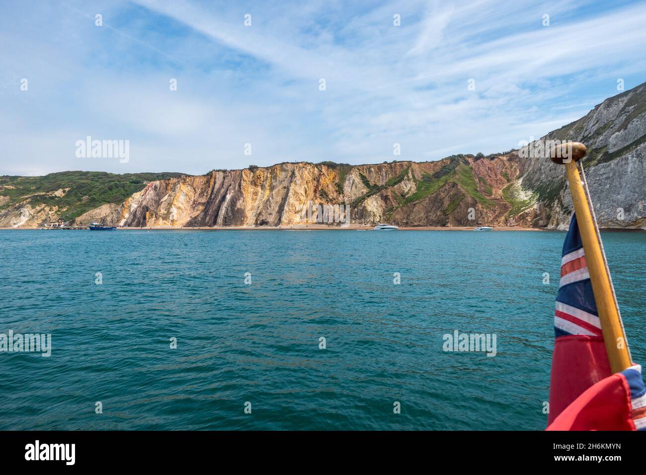 Boats moored in alum bay with its multi-coloured sand cliffs with English red ensign flag on flagestaff in the foreground,  Isle of Wright Hampshire Stock Photo