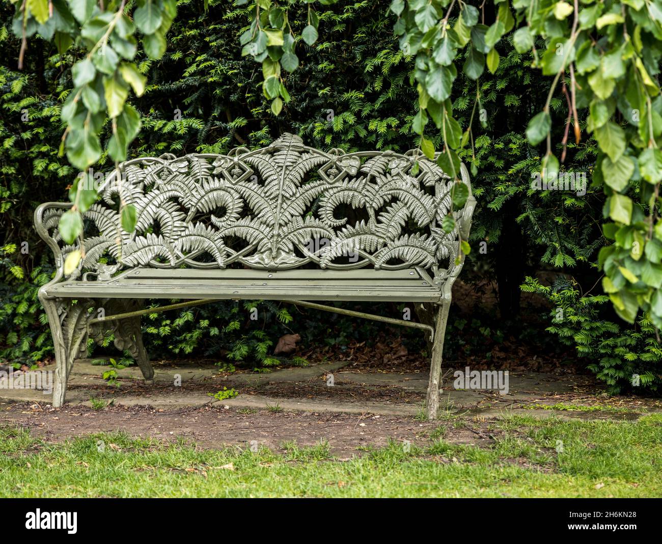 Posh park bench decorated with fern palms in pretty garden setting England Stock Photo