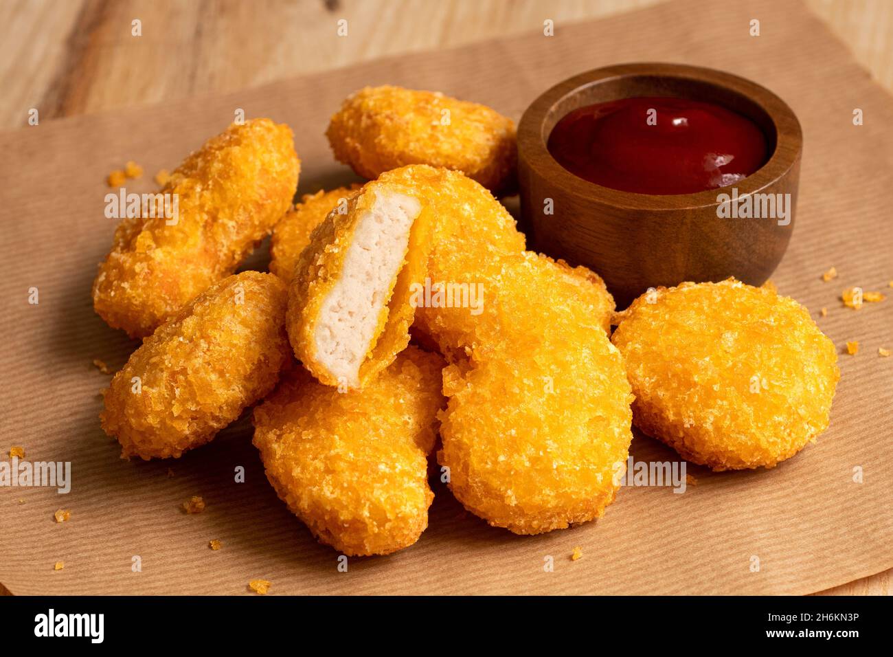 Fried gluten free cornflake crumb chicken nuggets next to a wood bowl of ketchup on brown baking paper. Stock Photo
