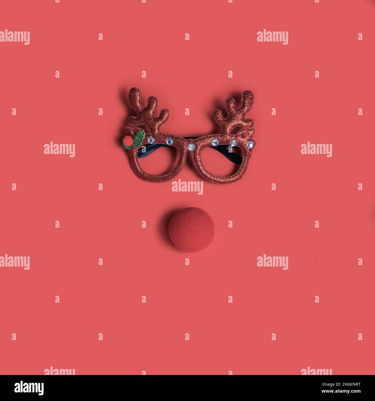Christmas face with festive glasses and a clown nose on a red background. Flat lay. Stock Photo