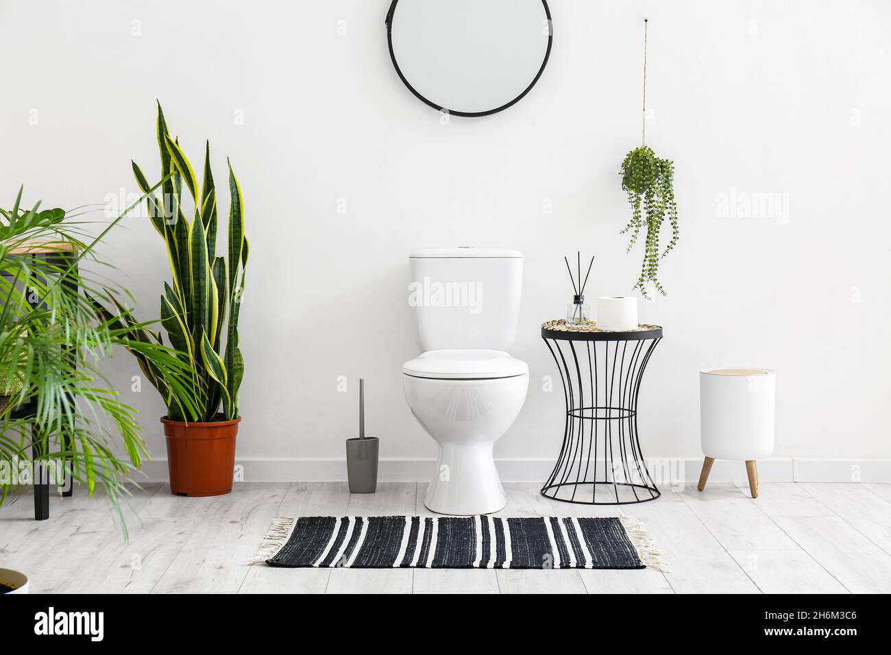 Toilet bowl, houseplants and table with bathroom accessories near white