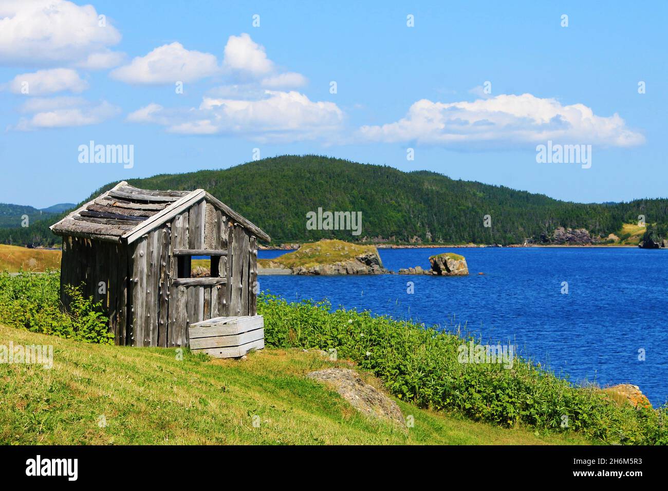 An old, weathered outbuilding on a grassy hill by the side of the bay