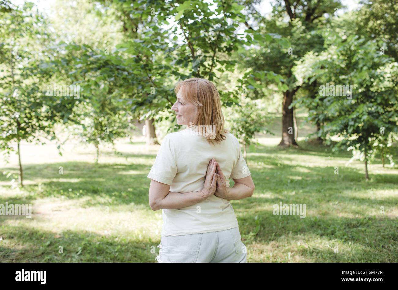 a woman does yoga in an outdoor park with her arms crossed behind her ...