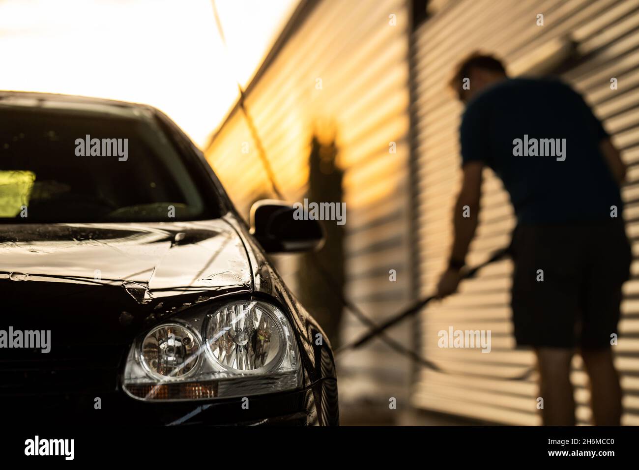 Young man washing his beloved car carefully in a manual car wash to