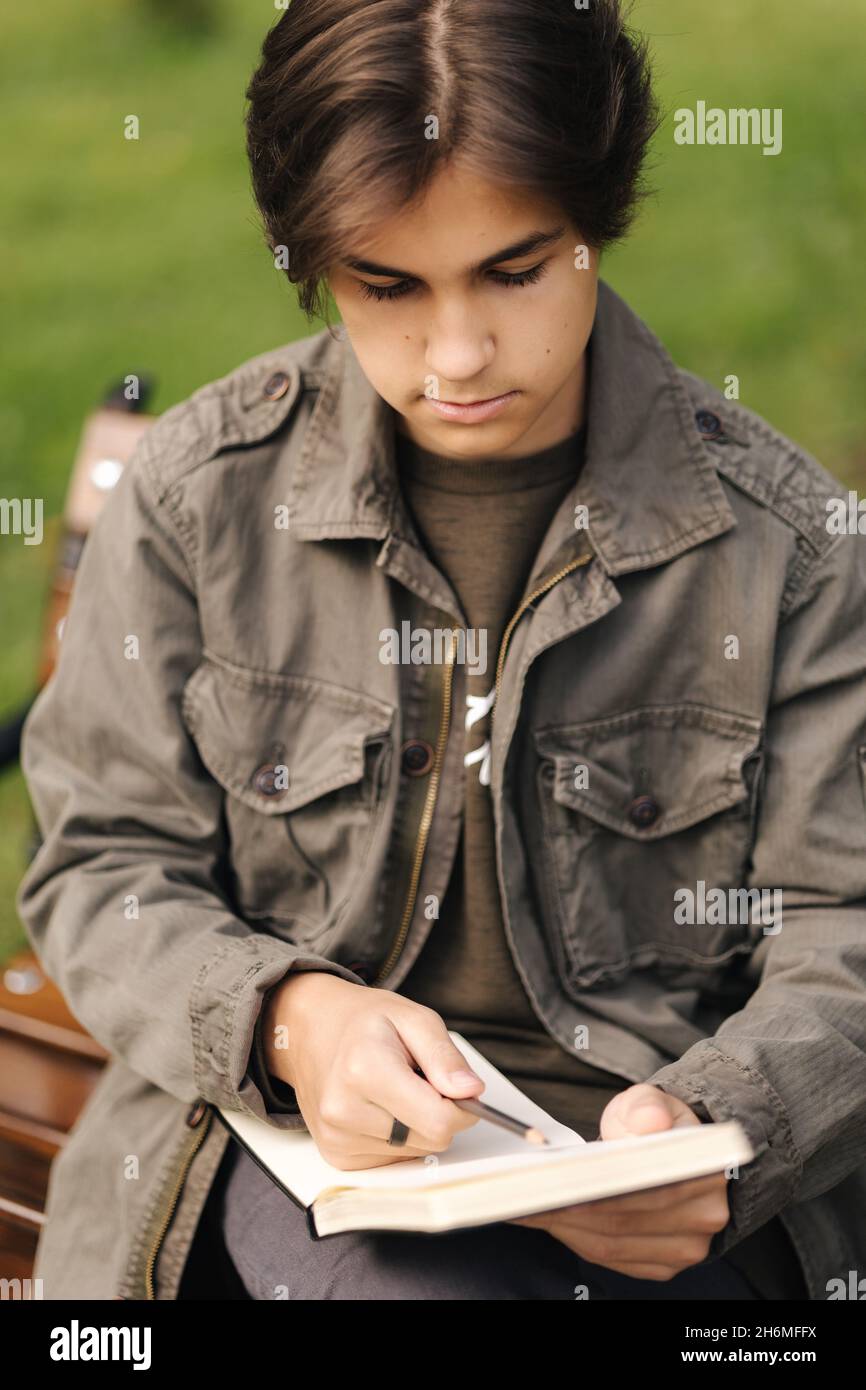 Handsome teenager painting something in his notepad outdood during the break. Talanted young boy Stock Photo
