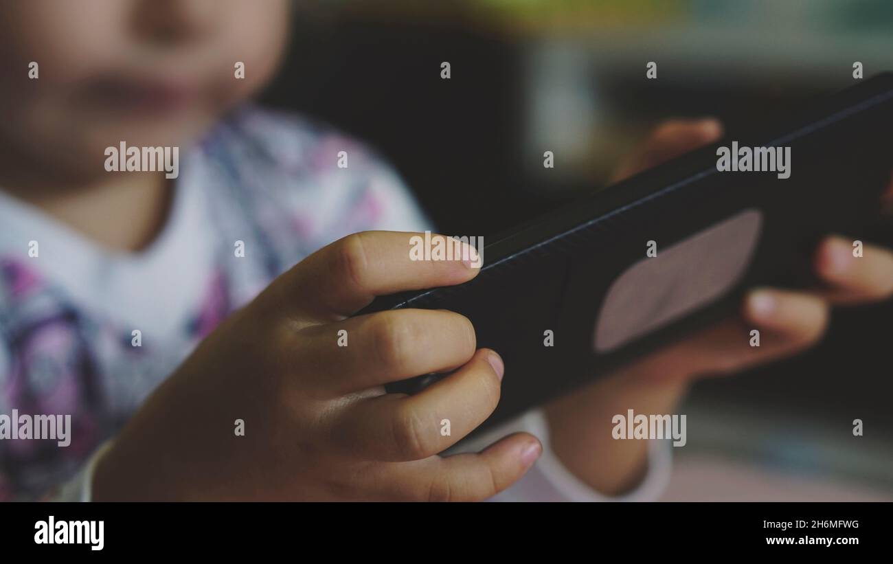 Little child playing with a mobile phone. Concept of harmful habits, screen time, and bad parenting. Entertainment of the homeschooling and e-learning Stock Photo