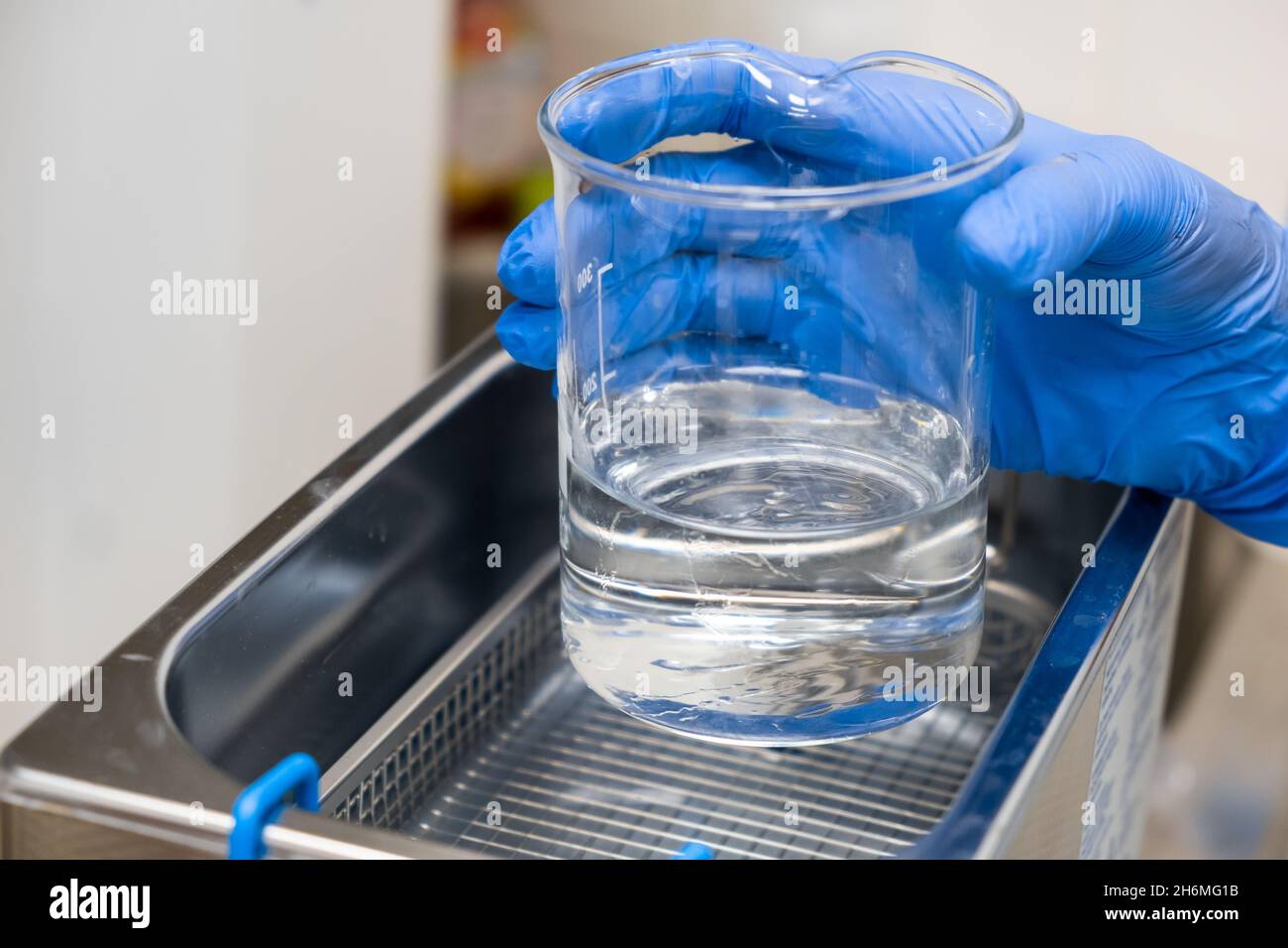 Scientist in blue rubber puts a beaker for dissolving or cleaning into