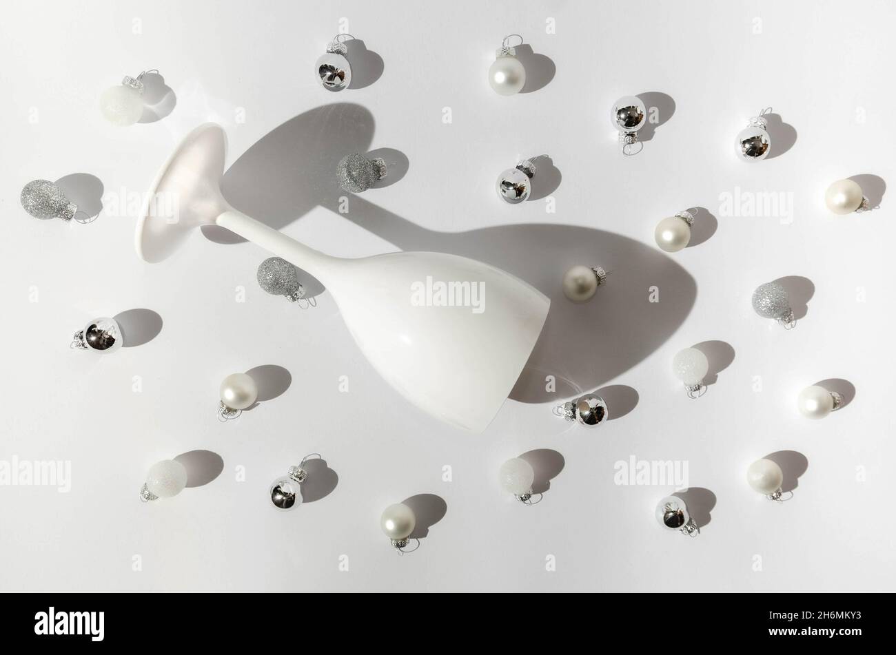 A white wine or Champagne glass on white background with small white and silver Christmas decoration balls. Festive all white creative concept for Chr Stock Photo