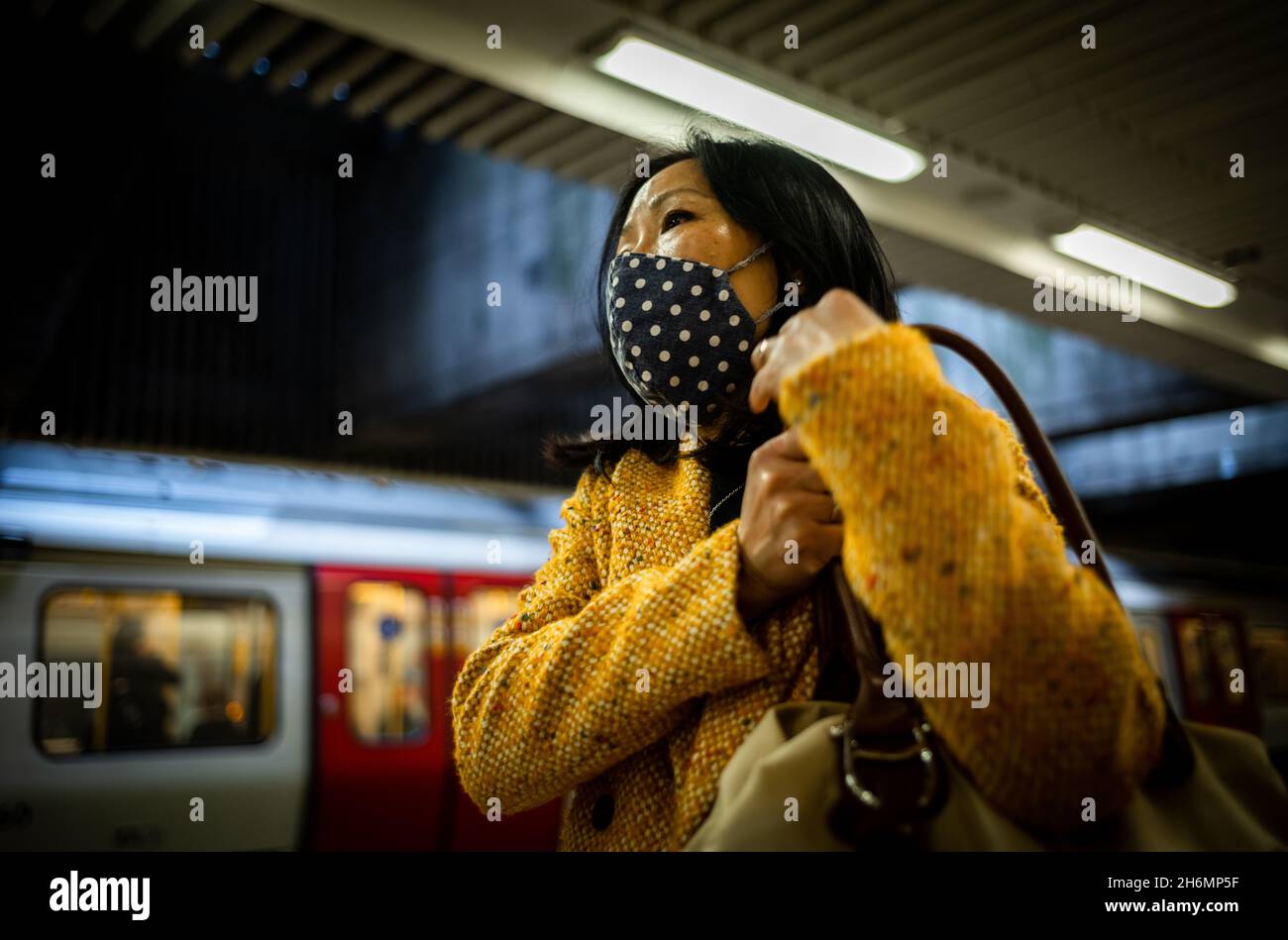 An Asian woman wearing a face mask waits for a train on the London Underground. Face masks were compulsory on the tube due to the coronavirus Covid-19 Stock Photo