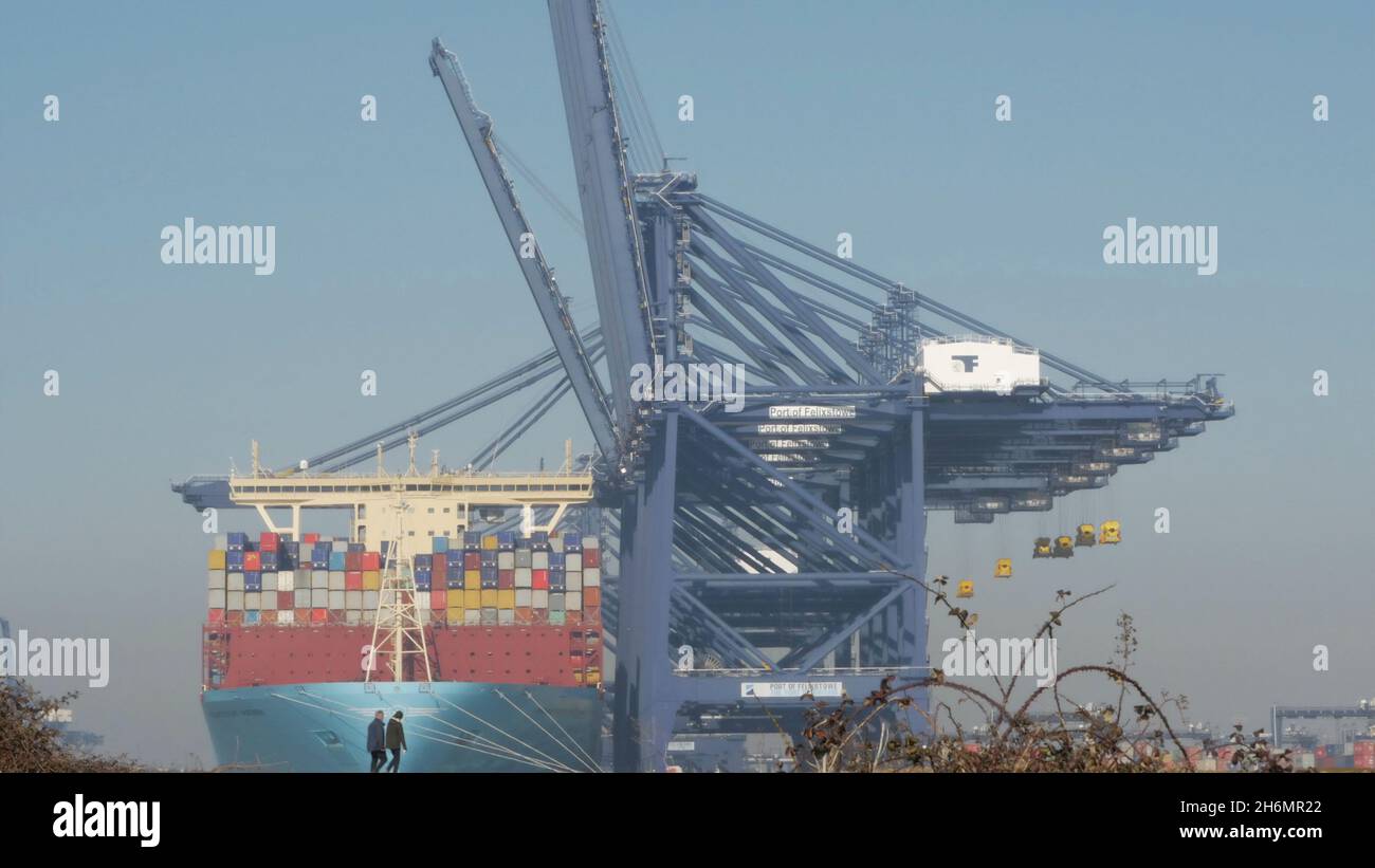 Couple walking with a giant container ship berthed at the Port of Felixstowe, from Landguard Point, River Orwell, Suffolk, England, United Kingdom Stock Photo