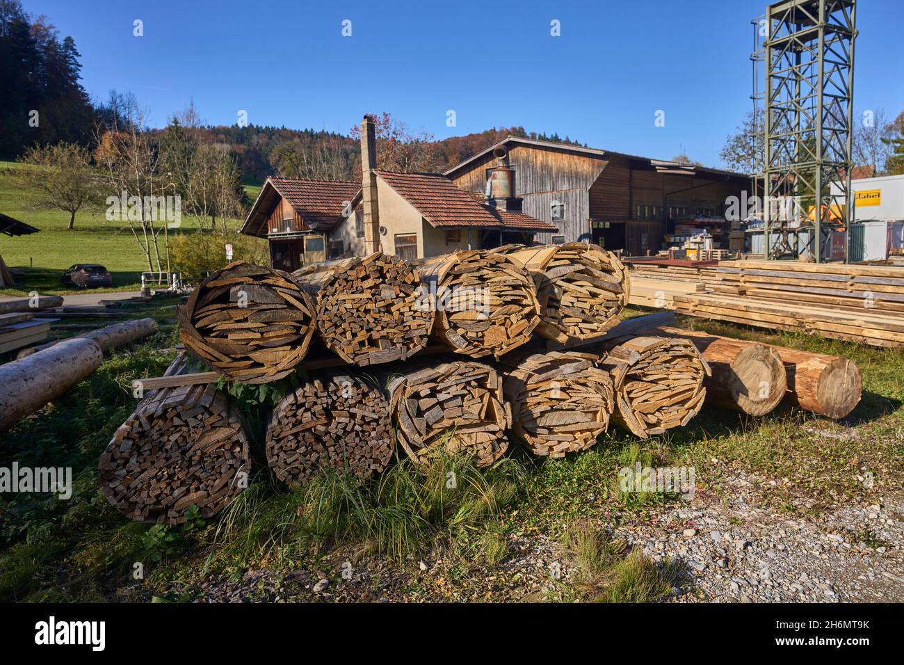 Outdoor Lumber Yard, In The Background Sawmill Building, Meadow And Blue Sky. Gündisau, Zurich Oberland, Switzerland Stock Photo