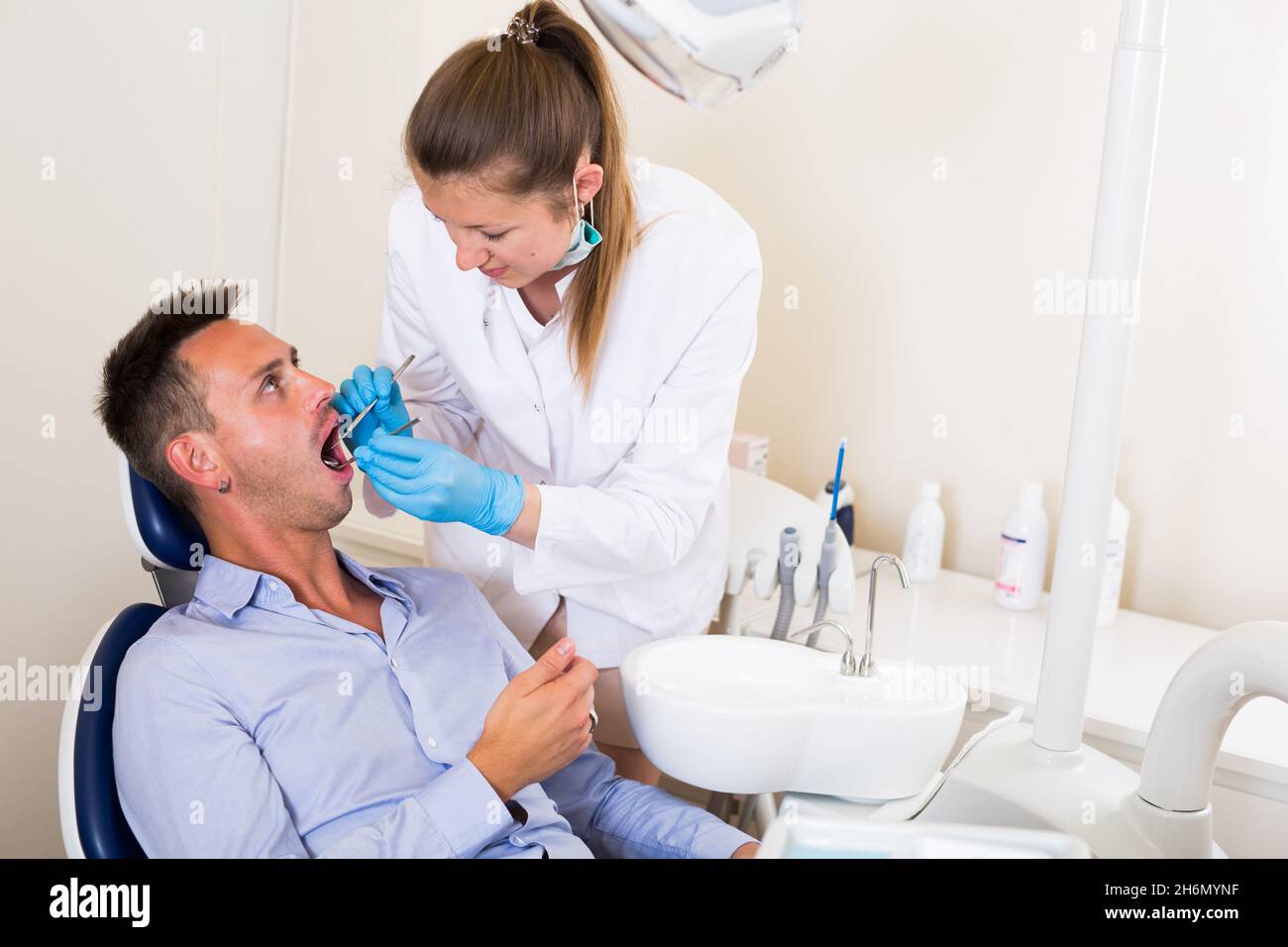 Dentist in uniform is taking examination of a young male Stock Photo