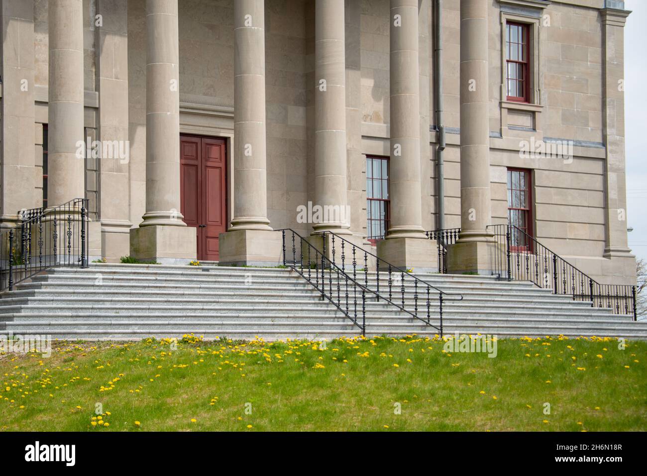 The exterior facade of a historic government building with large vintage marble pillars or columns, red door, black rails, and a brick entrance Stock Photo