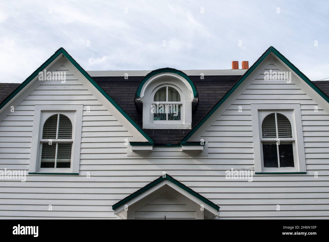 A white wood clapboard siding vintage house with multiple windows. The center window has a curved dormer over the closed glass window in the black Stock Photo