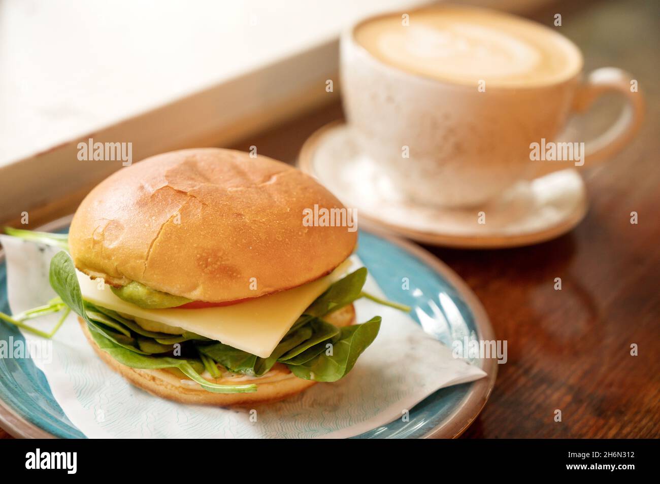 Vegetarian breakfast sandwich with cappuccino coffee drink at a trendy coffee shop. Stock Photo