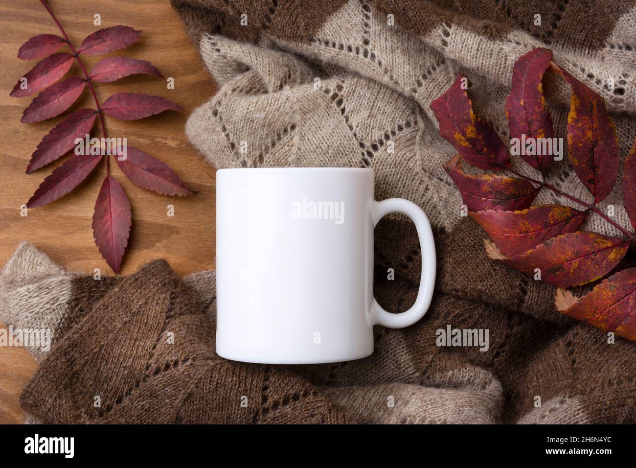 White coffee mug mockup with knitted blanket and red fall rowan leaves.  Empty mug mock up for design promotion, styled template Stock Photo