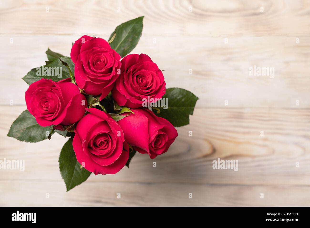 Beautiful bouquet of five red roses with leaves on wooden background top  view. Copy space. Concept for congratulations and wishes Stock Photo - Alamy