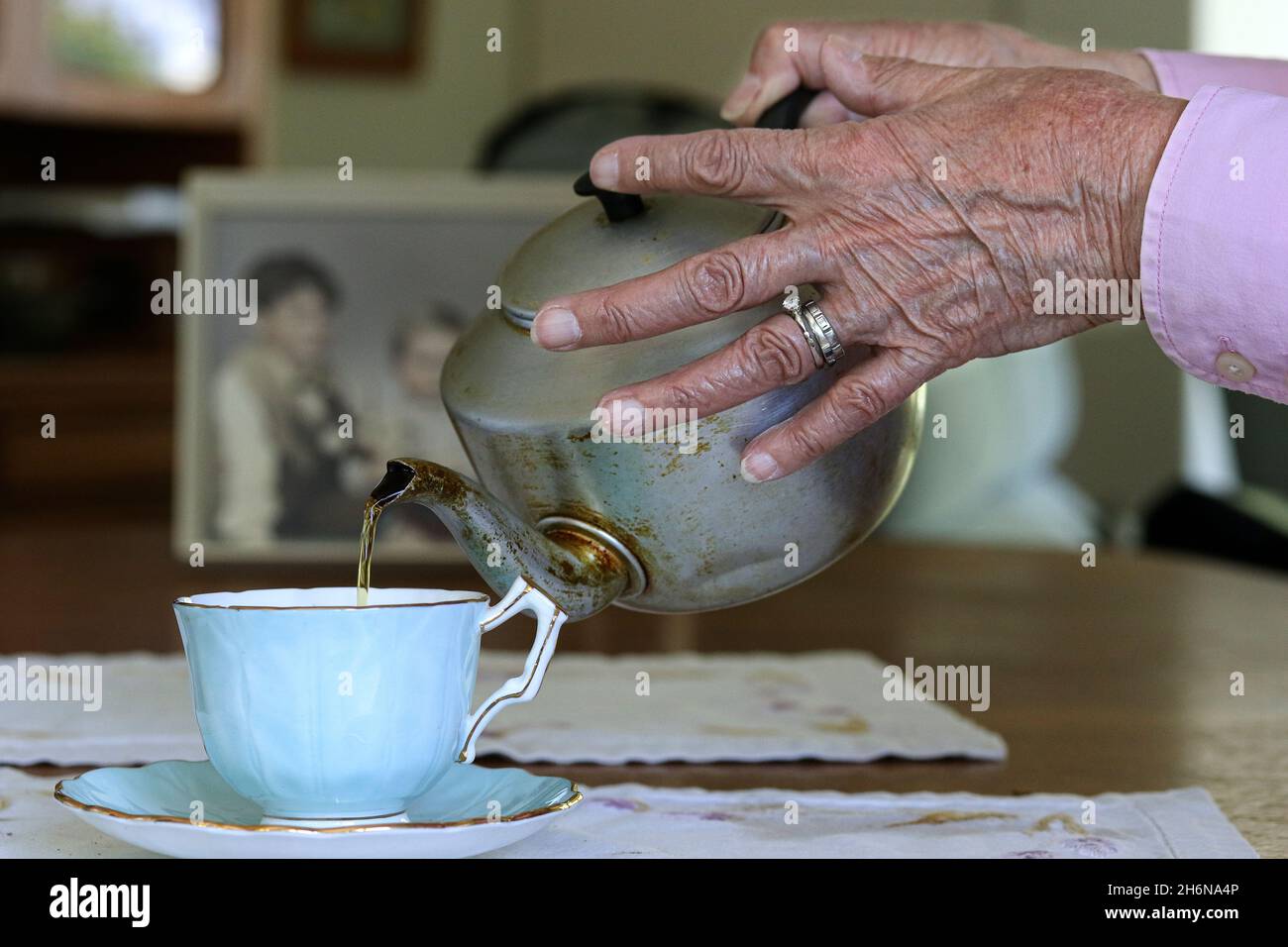 Generic photo of a females old hands pouring a cup of tea from a pot into a china cup. Stock Photo