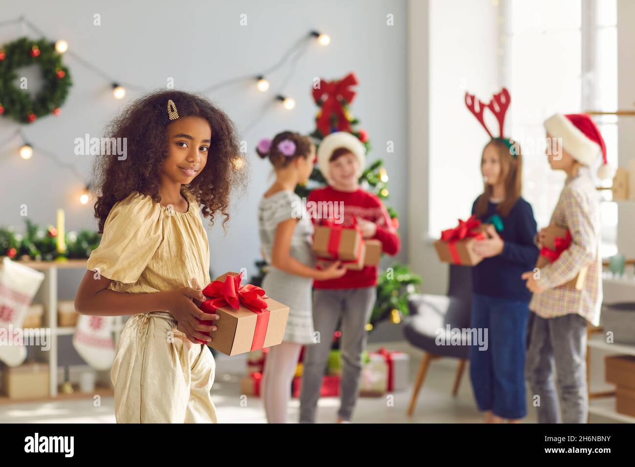 Smiling african american girl with a Christmas present in her hands stands in a bright room. Stock Photo