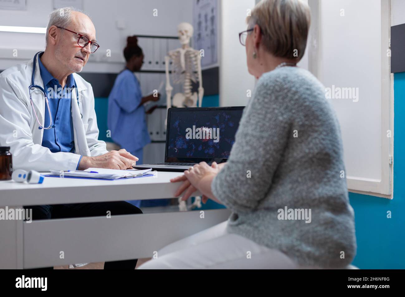 Man doctor explaining coronavirus bacteria illustration on laptop to woman in cabinet. Medical specialist and patient looking at computer screen with visual representation of covid 19 pandemic. Stock Photo