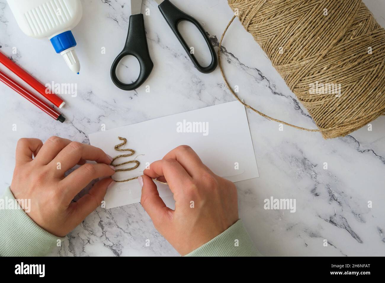 https://c8.alamy.com/comp/2H6NFAT/diy-ribbon-rope-scissors-used-to-create-individual-greeting-card-merry-christmas-christmas-tree-made-of-rope-top-view-of-hands-making-step-by-step-2H6NFAT.jpg