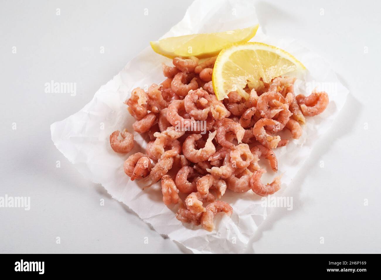 From above of heap of cooked peeled Krabben with slices of fresh lemon on baking paper on white background Stock Photo