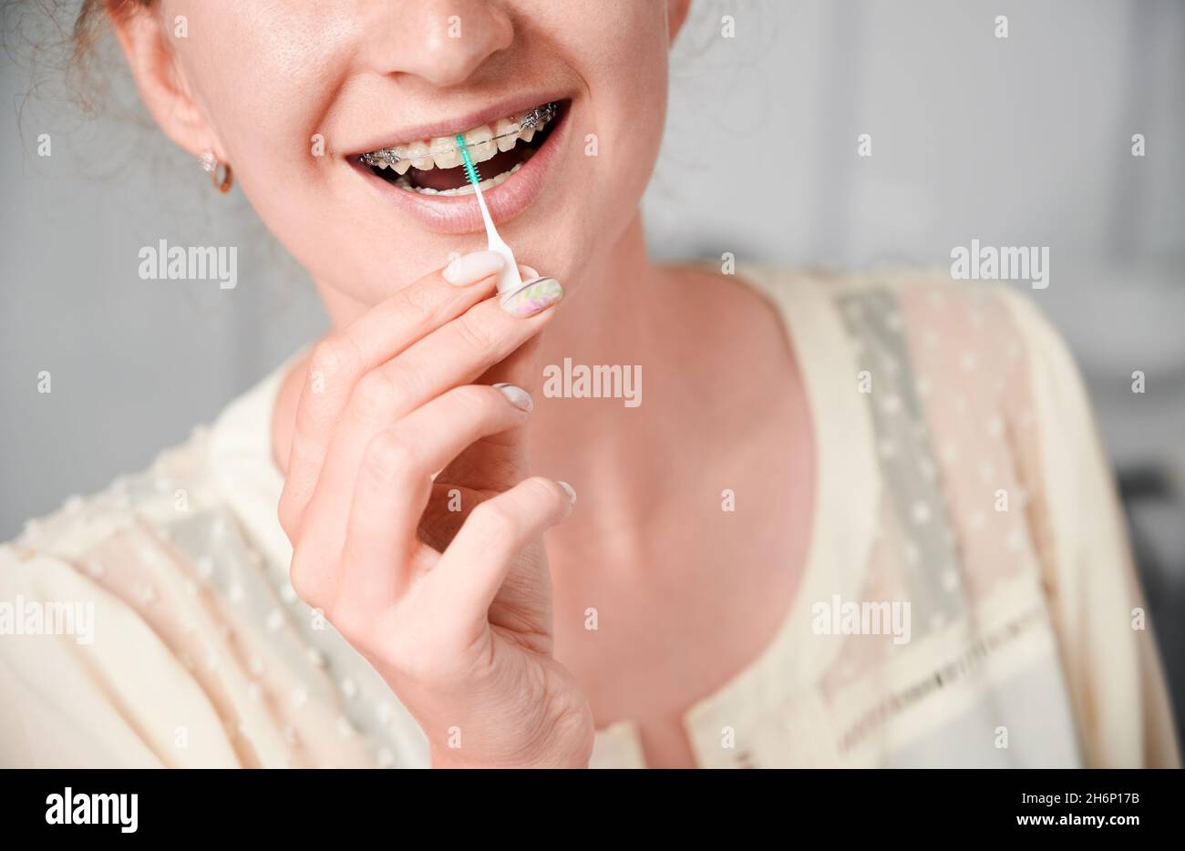 Close up of smiling young woman using dental floss brush while cleaning