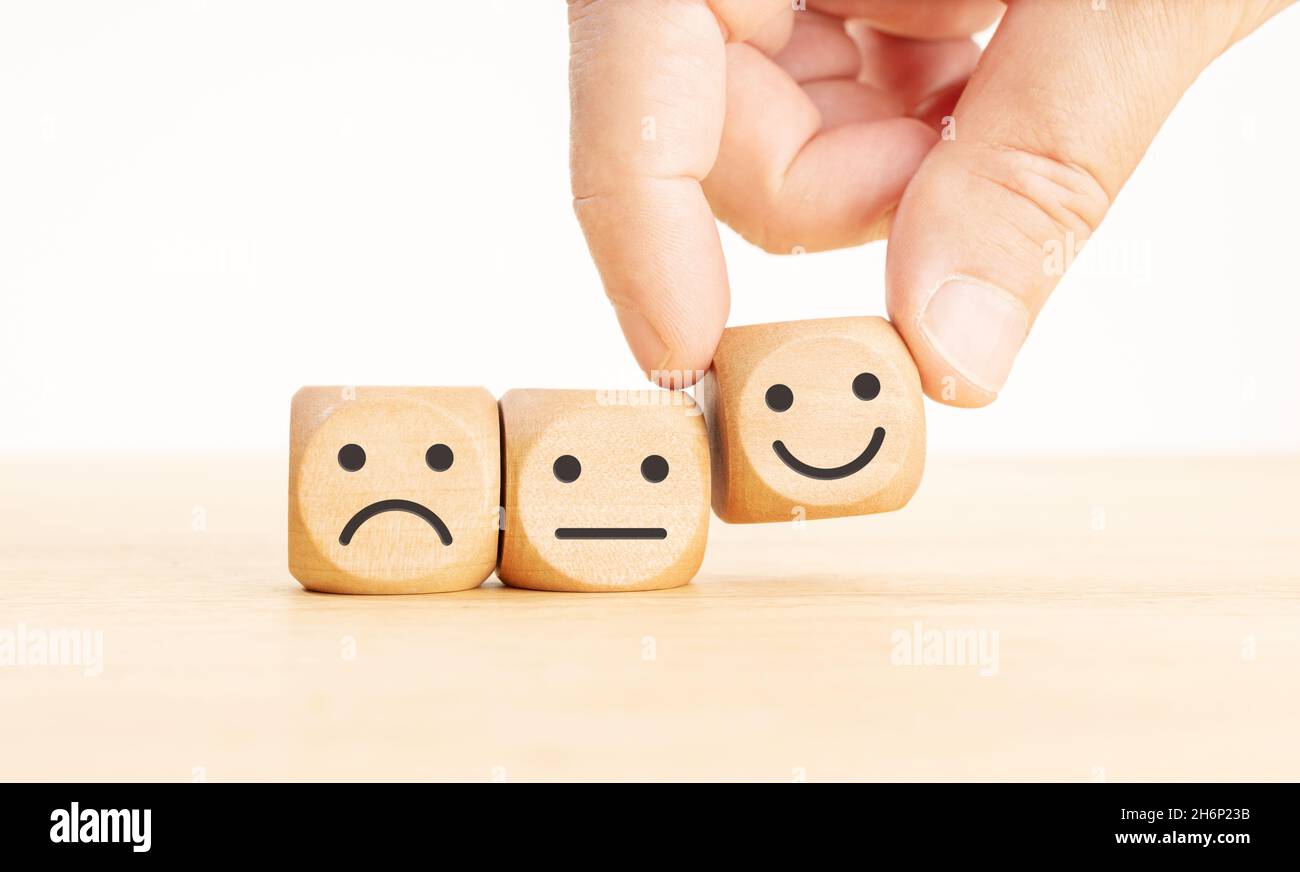 Customer service evaluation concept. Hand picking the happy face emoticon on wooden block Stock Photo