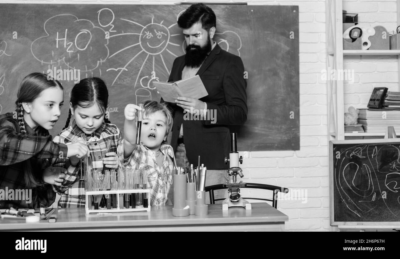 happy children and teacher. doing experiments with liquids in chemistry lab. chemistry lab. back to school. kids in lab coat learning chemistry in Stock Photo