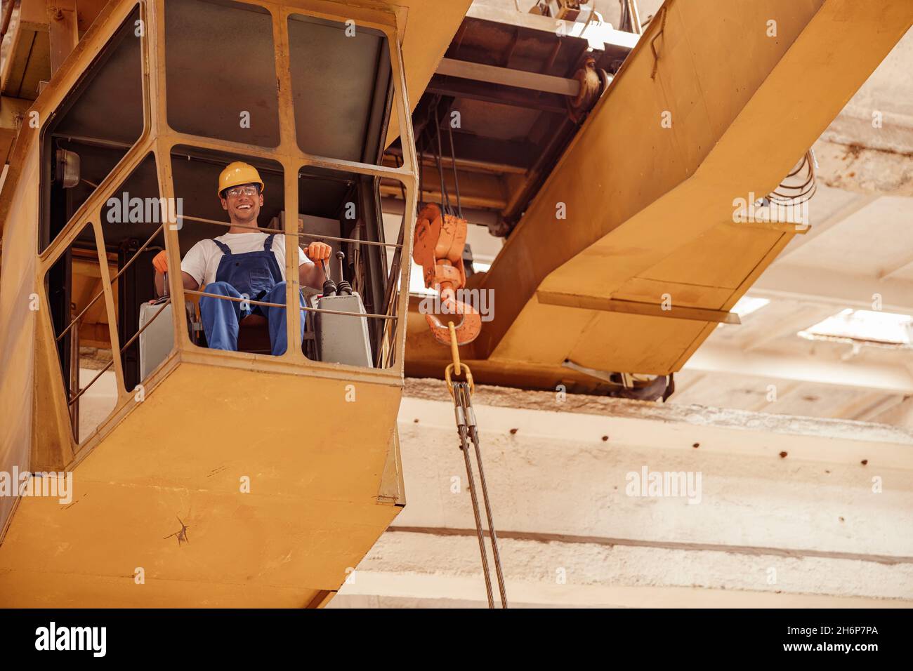 Cheerful man sitting in operator cabin of overhead crane Stock Photo