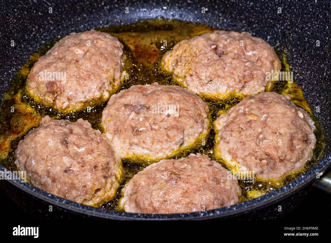 Raw white fish meat cutlets, heated in a ceramic black skillet with ...