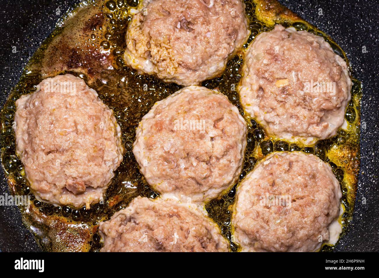 Raw white fish meat cutlets, heated in a ceramic black skillet with ...