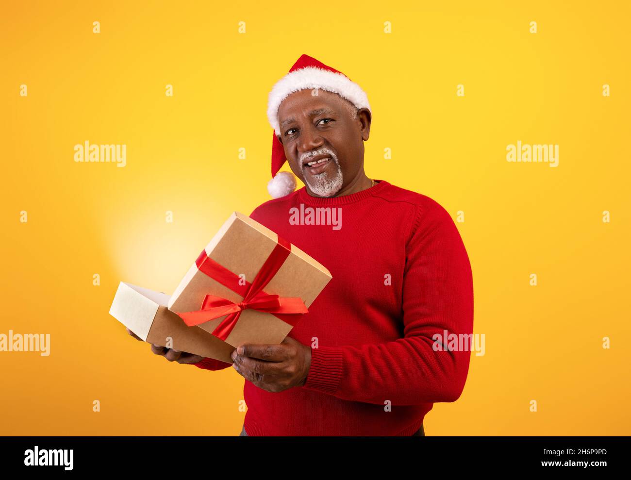 Happy senior black man in Santa hat opening Xmas gift with fairy light, receiving desired present for Christmas Stock Photo