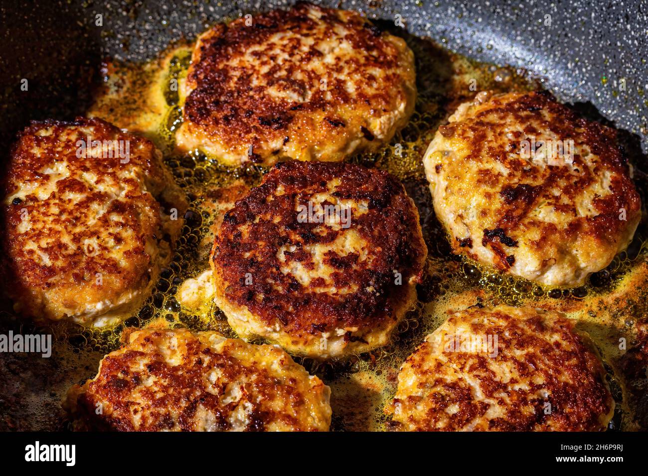 Raw white fish meat cutlets, heated in a ceramic black skillet with ...