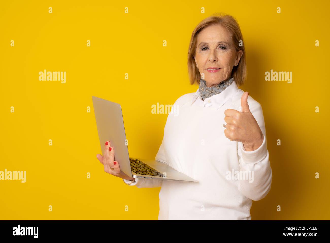 Mature woman holding laptop with thumb up isolated over yellow ...