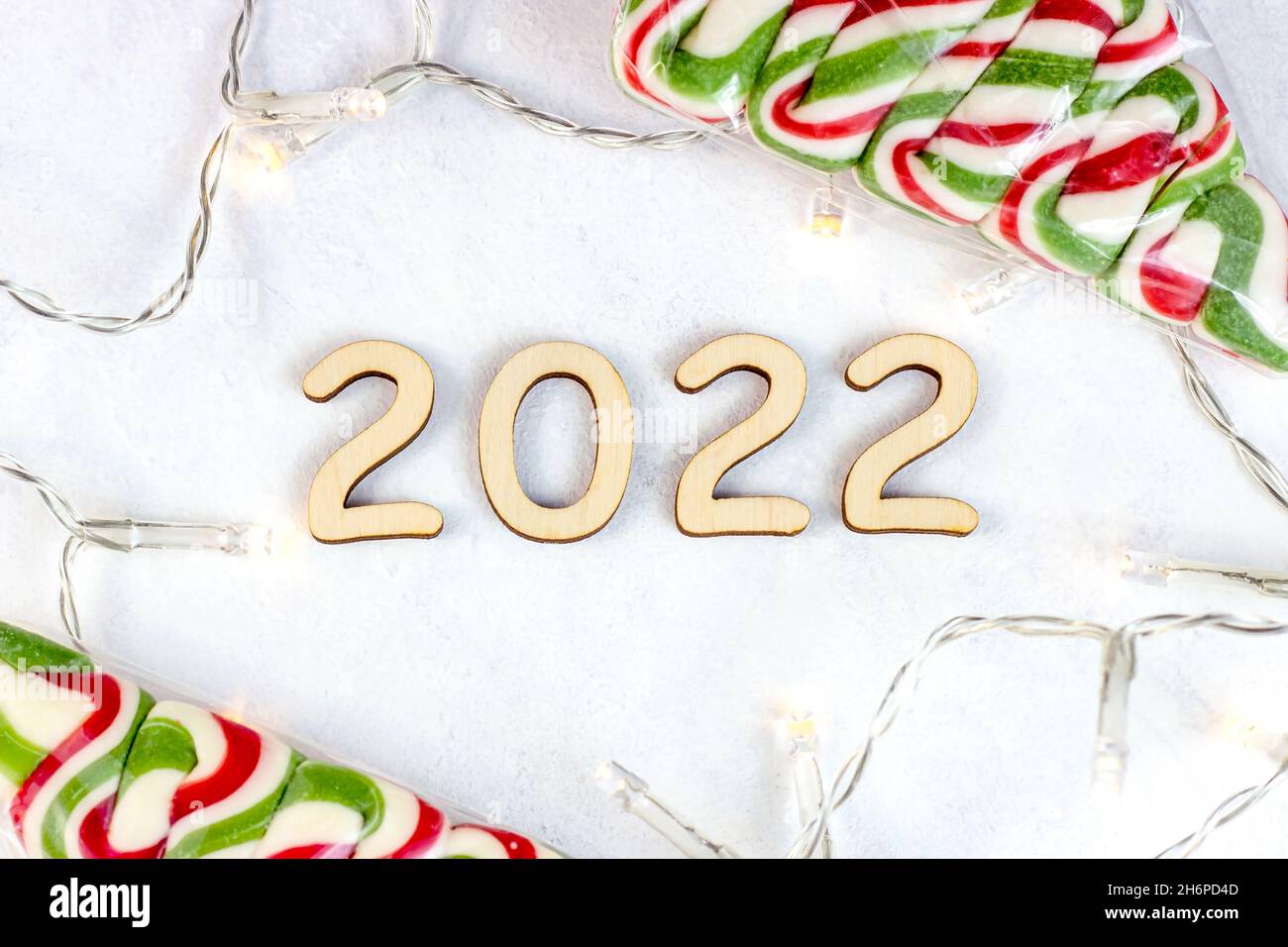 Top view of wooden numbers 2022 silhouette with Christmas lights and sweet candies on light background. New Year beginning congratulations and plannin Stock Photo