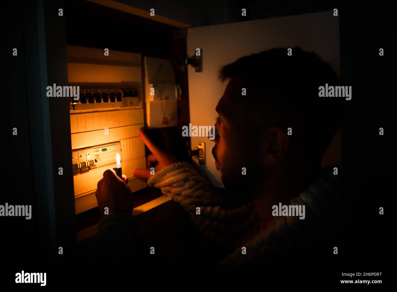 Man with lighter in total darkness investigating fuse box or electric switchboard at home during power outage. Blackout, no electricity concept Stock Photo