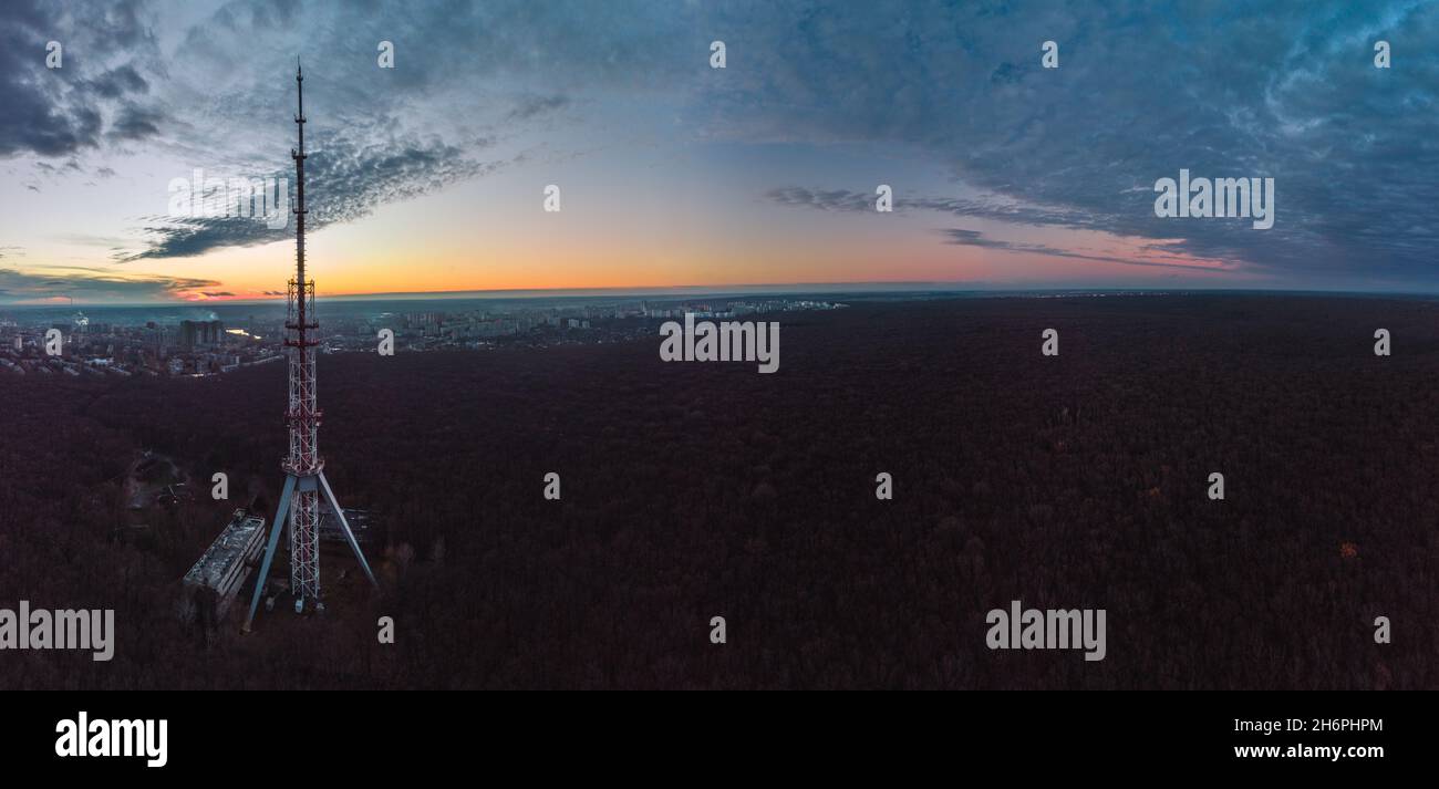 Aerial panorama at sunset, evening view on dark forest with telecommunication tower antenna silhouette and scenic cloudy sky. Kharkiv, Ukraine Stock Photo