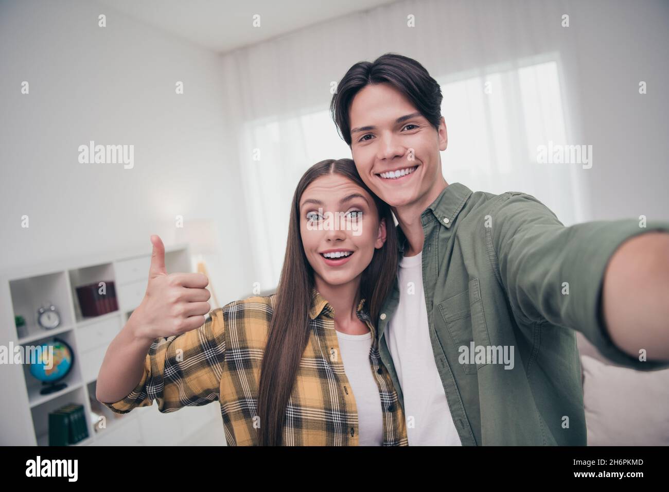 Photo of attractive beautiful young couple wear casual outfits smiling  cuddling showing thumb up recording self video indoors house room Stock  Photo - Alamy