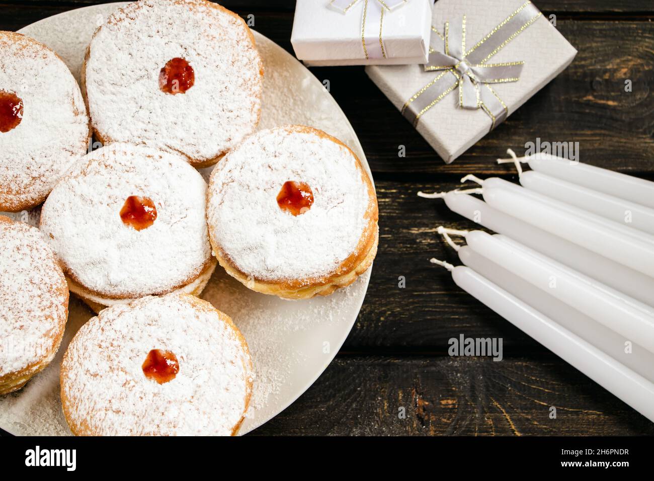 Happy Hanukkah. Traditional dessert Sufganiyot on dark wooden background. Donuts, candles and gifts. Celebrating Jewish religious holiday. Stock Photo