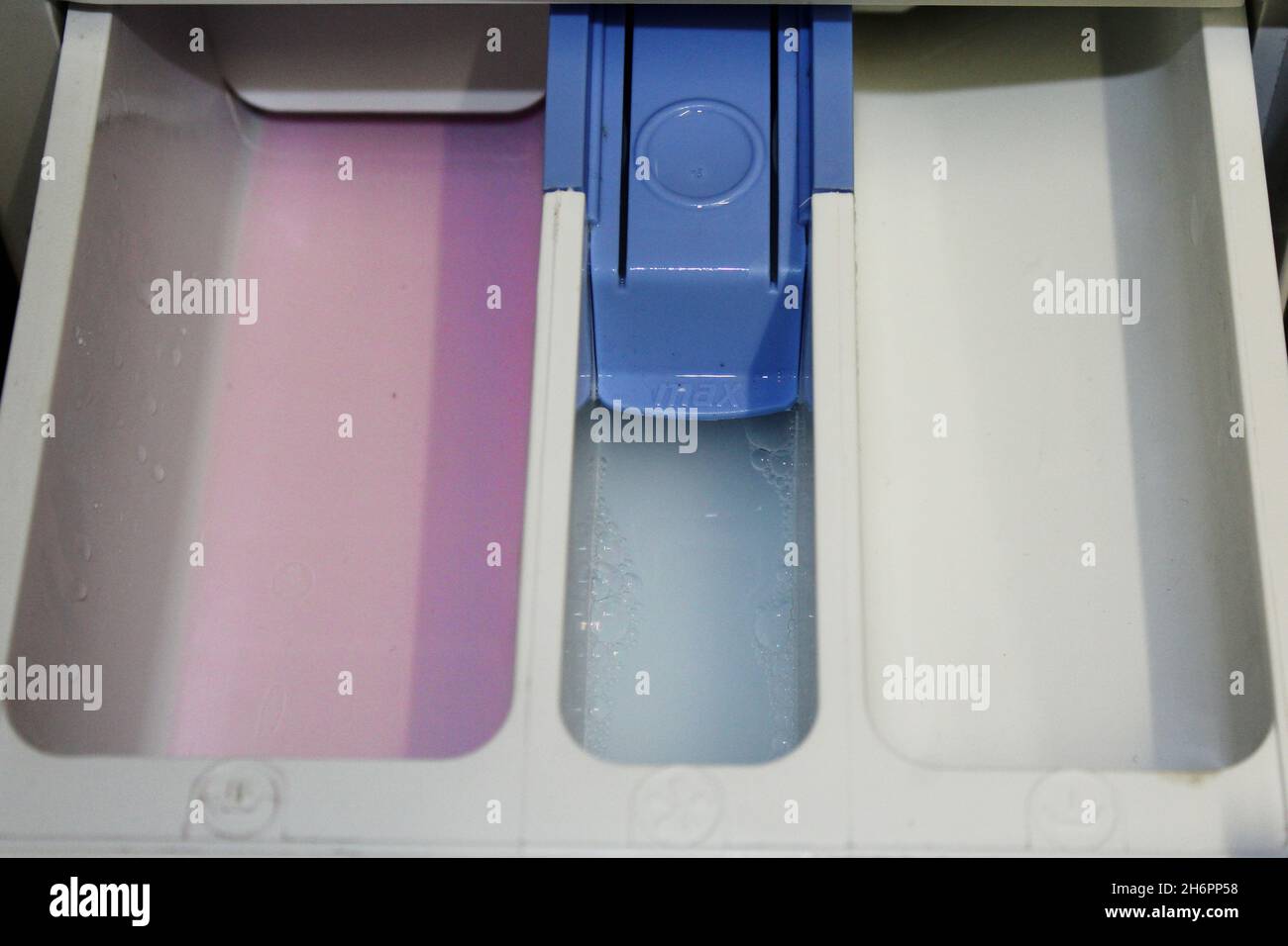 Nahaufnahme sauberer Waschmittelkammern / Waschmittelfächer einer Waschmaschine, gefüllt mit rosa Flüssigwaschmittel links & Weichspüler in der Mitte. Stock Photo