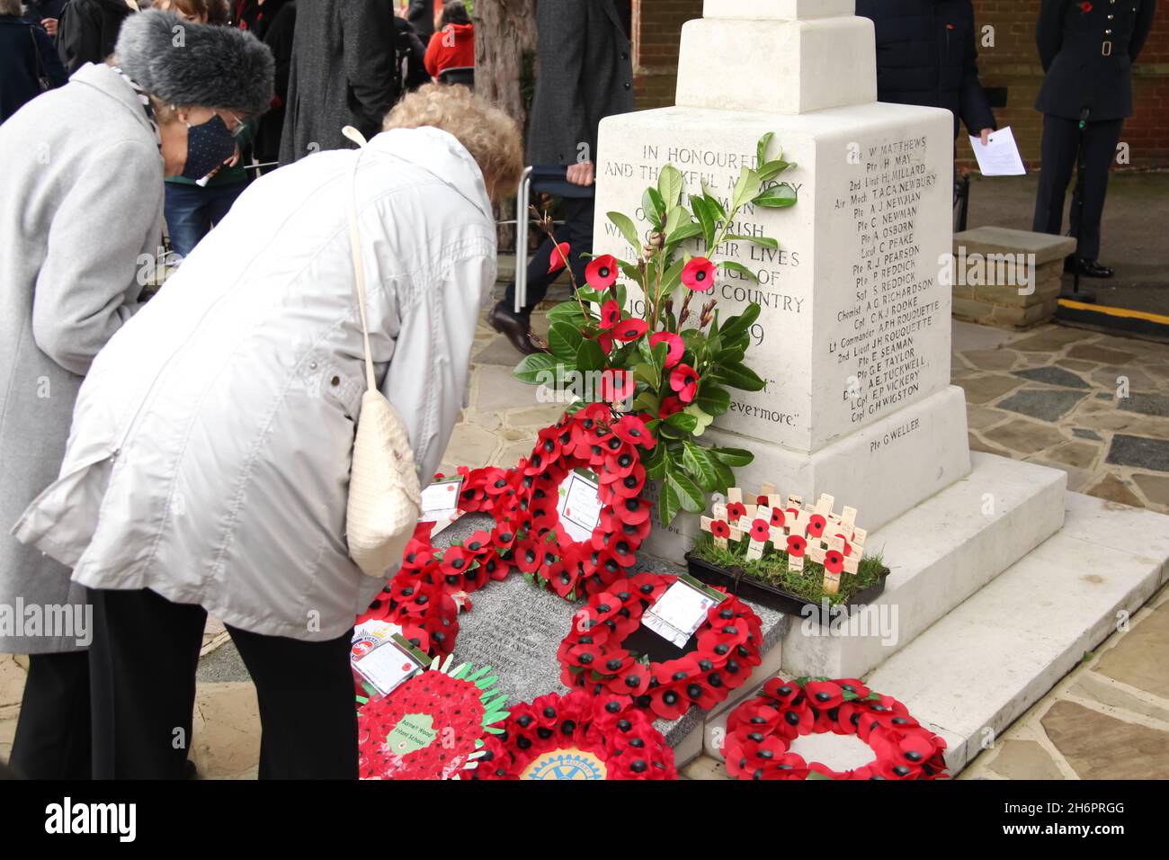 Two elderly ladies laying poppy wreath at war memorial on remembrance day, Ashtead, Surrey, England, 2021 Stock Photo