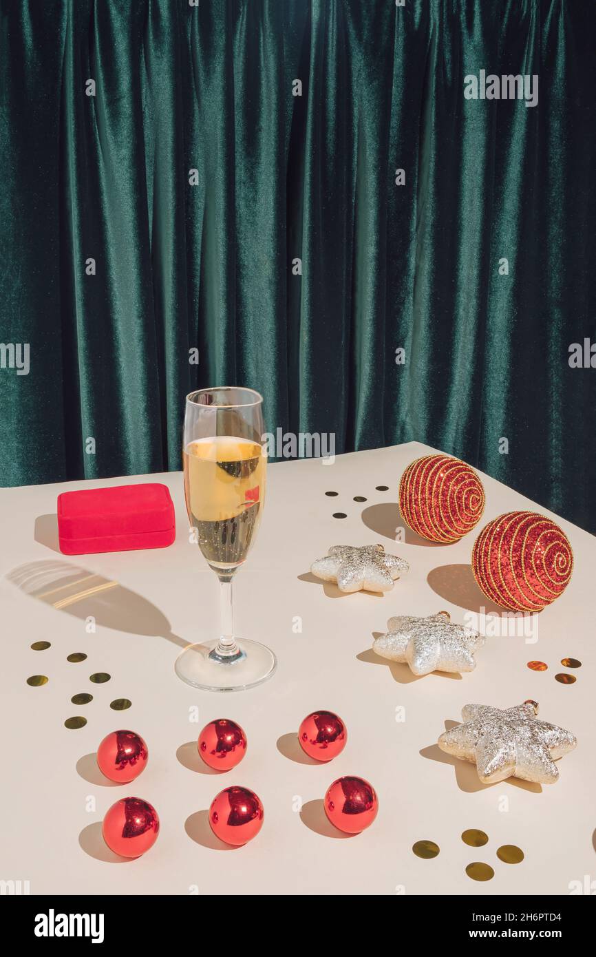 Creative retro aesthetic concept. Minimal New Year party composition with jewelry box, champagne glass, confetti and red Christmas baubles. Modern hol Stock Photo