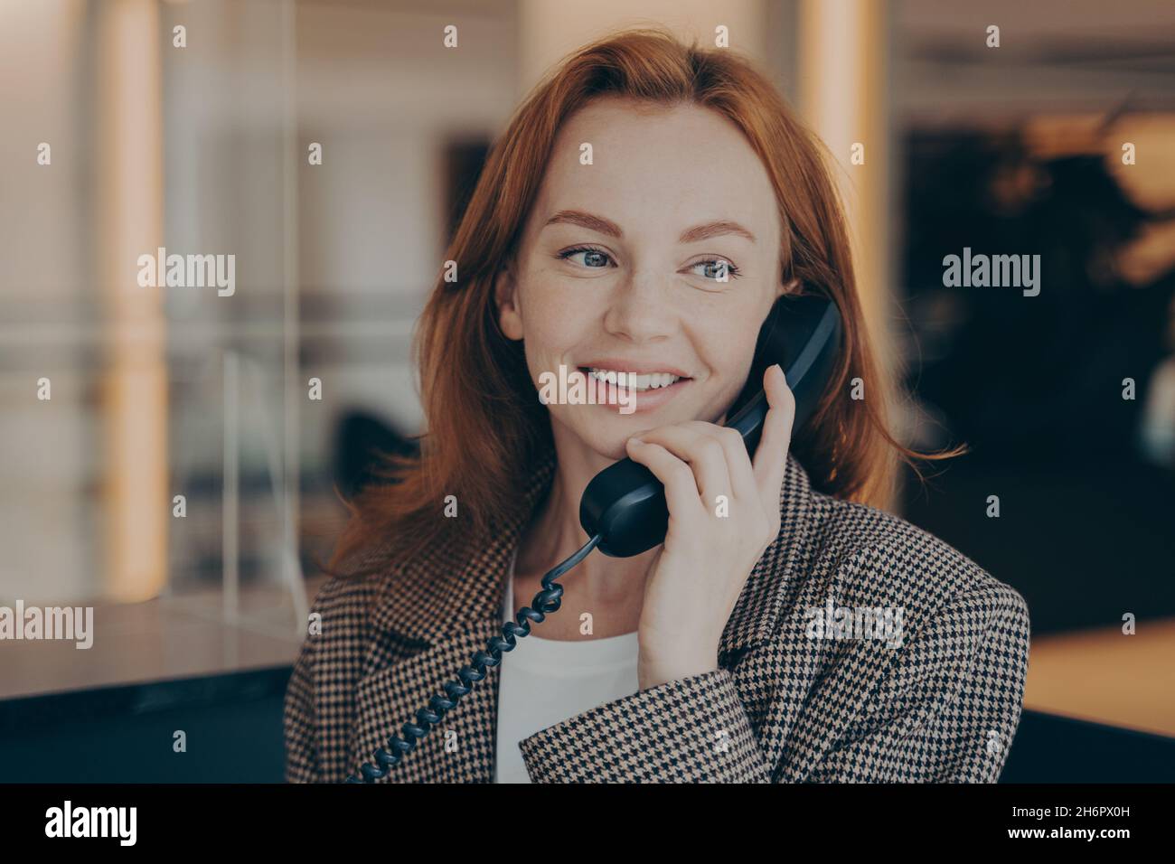 Portrait of satisfied female office worker using black landline phone, calling business partner Stock Photo